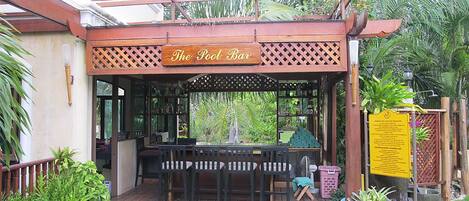 Un bar junto a la piscina con asientos exteriores y un cartel arriba.