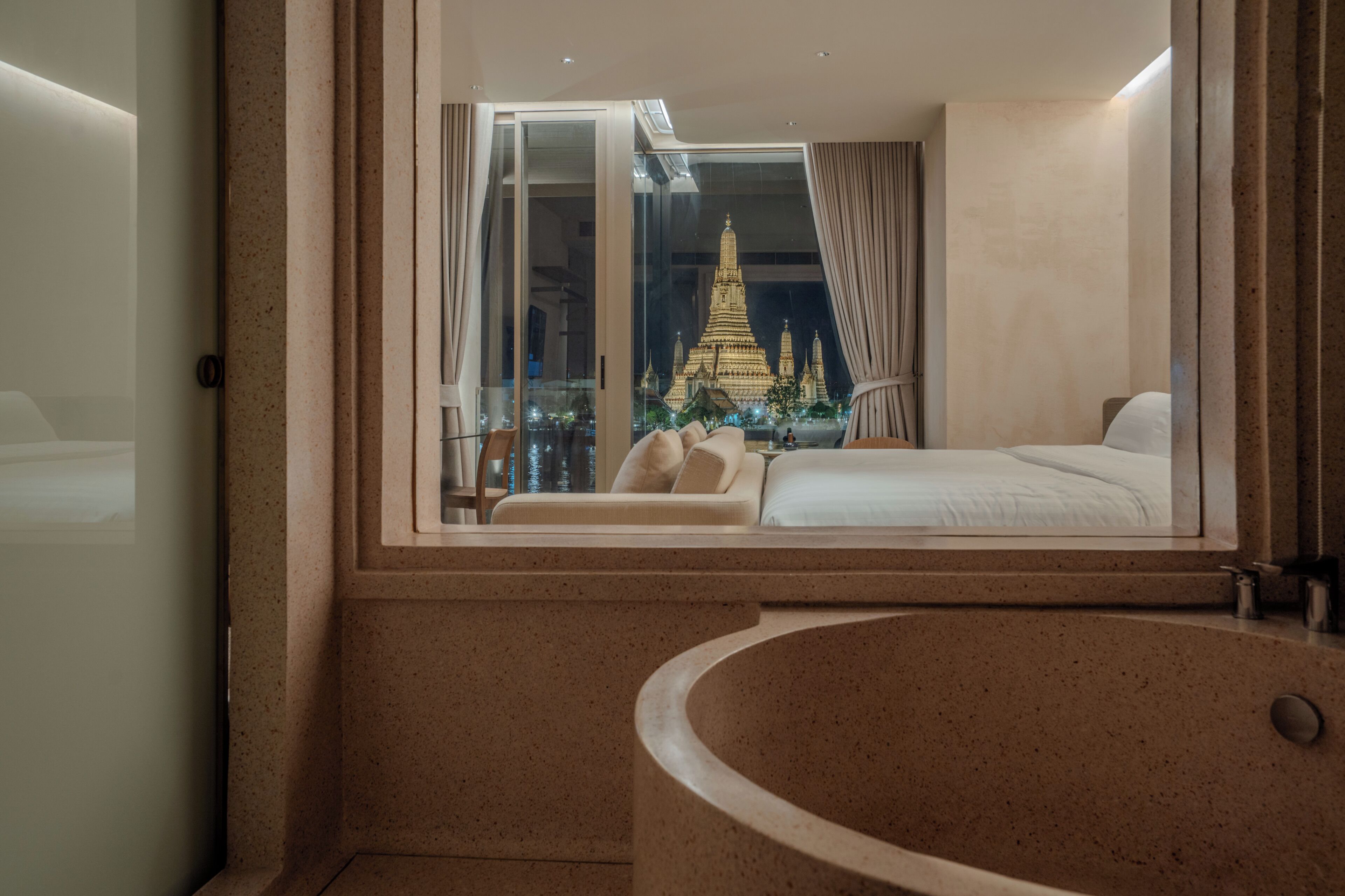 A modern hotel room with a large window, a bathtub, and a bed.