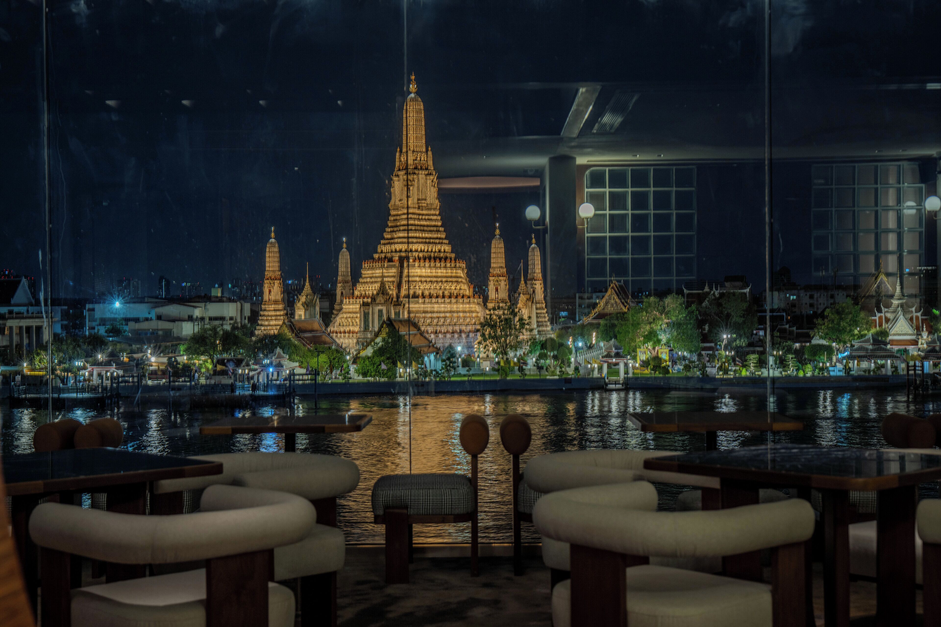 Vue nocturne d’un restaurant avec des tables et des chaises donnant sur un temple.