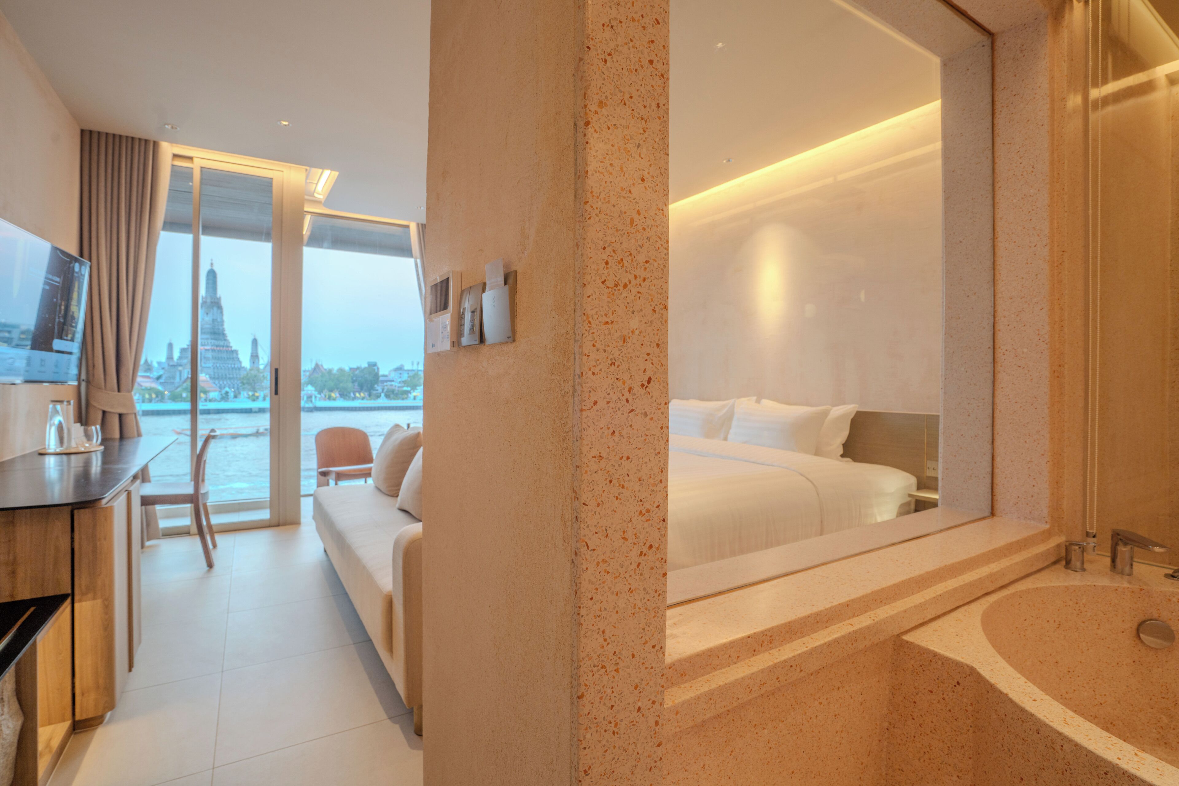 A hotel room with a large bed, a sitting area with a sofa and chairs, a TV, and a view of a temple through a large window.