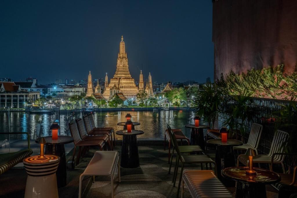 A rooftop bar with tables and chairs, overlooking a cityscape and a temple.