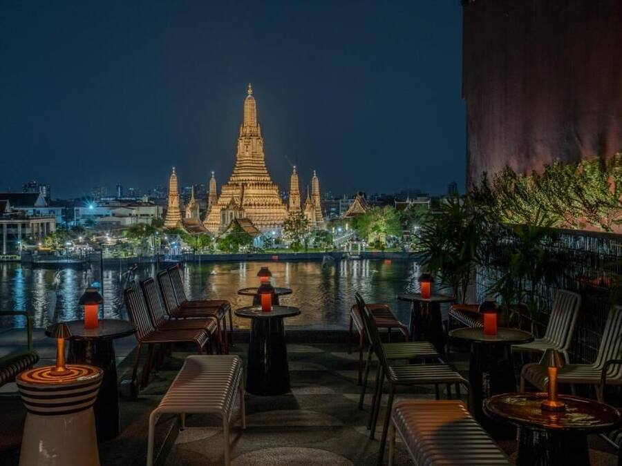 A rooftop bar with tables and chairs, overlooking a cityscape and a temple.