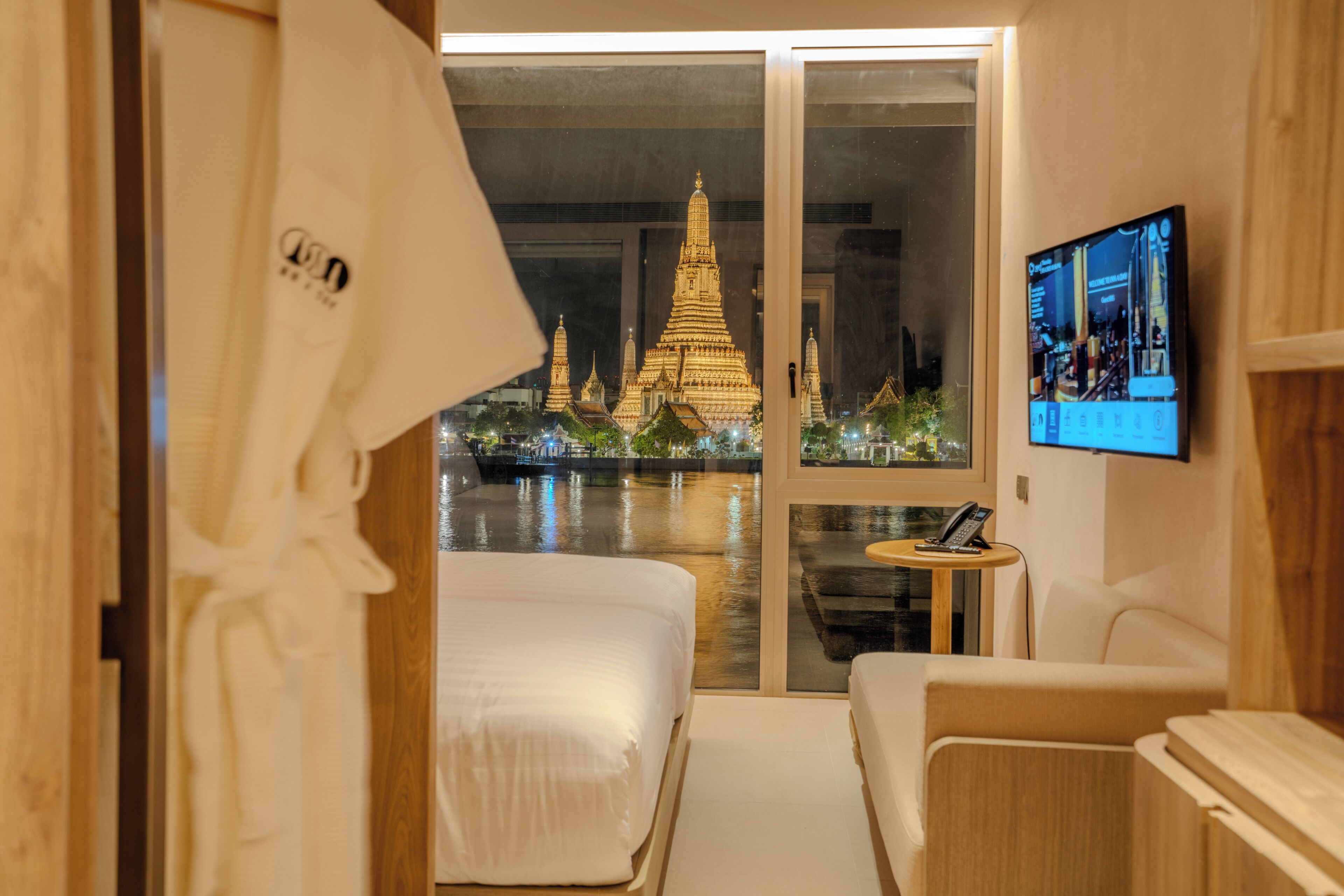 A hotel room with a bed, a sofa, a television, and a view of a temple at night.