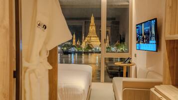 A hotel room with a bed, a sofa, a television, and a view of a temple at night.