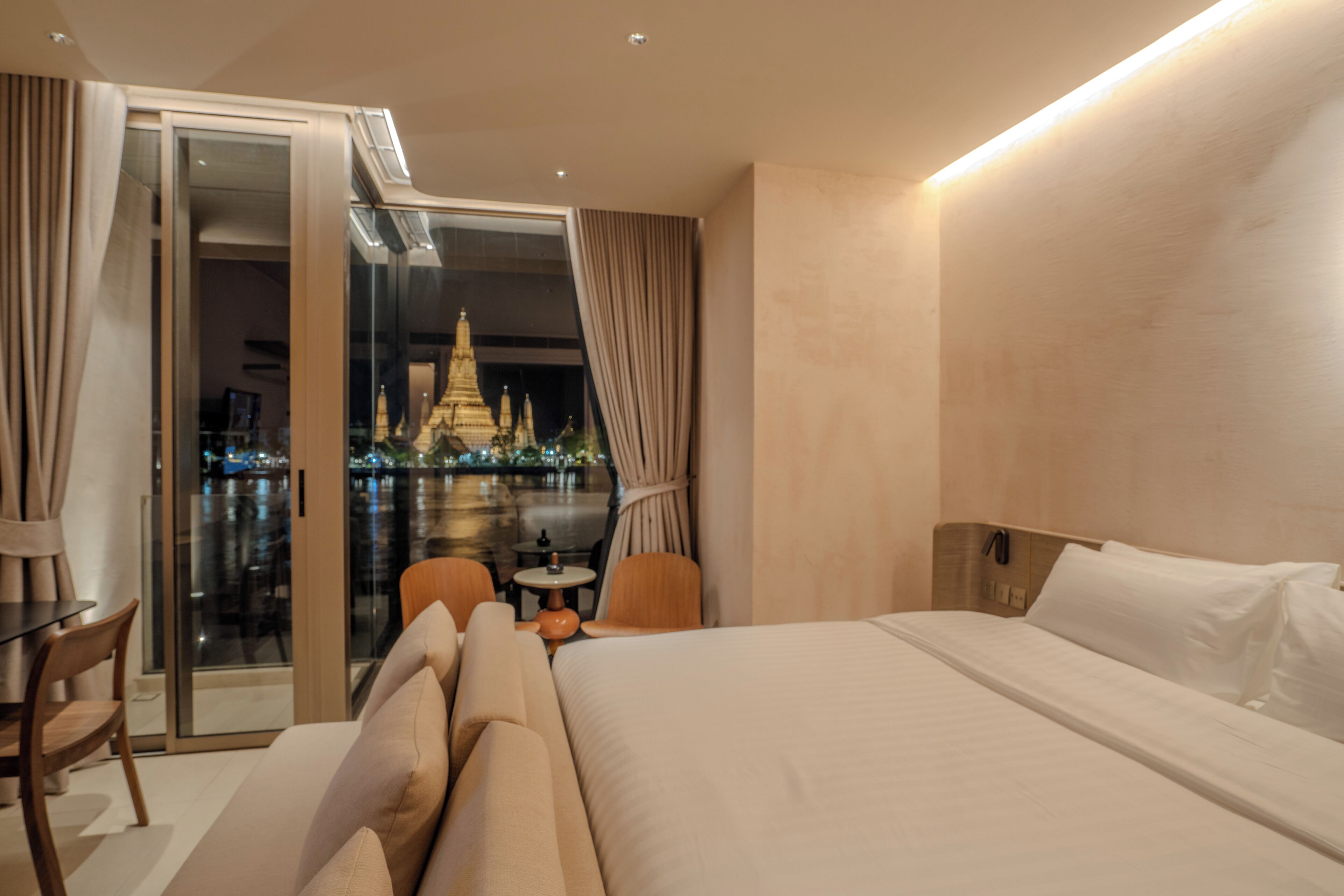 Quarto de hotel com cama, uma mesinha, cadeiras e vista para um templo por uma porta de vidro.
