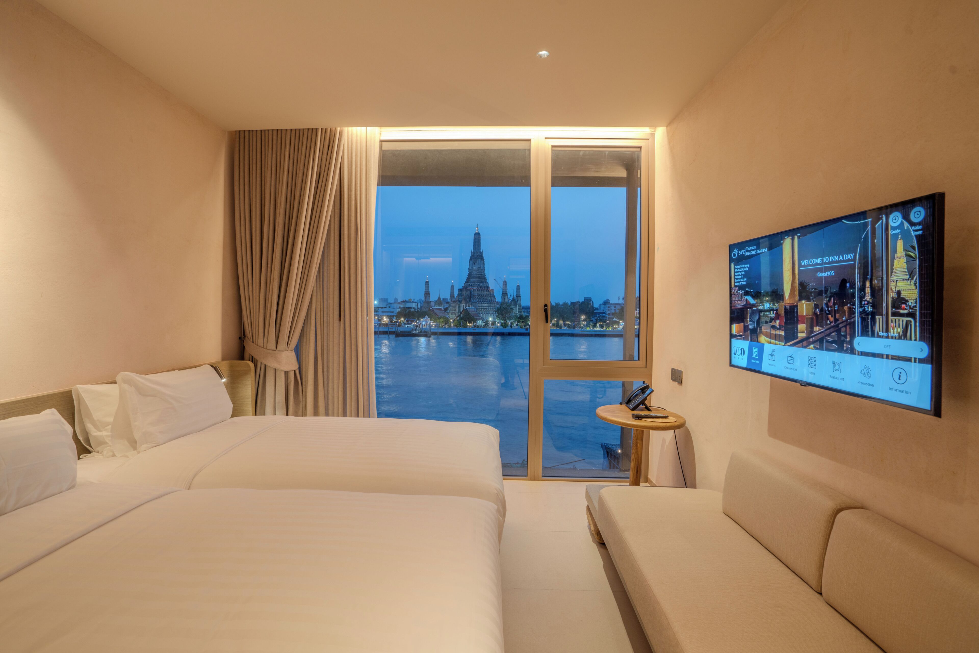 Ein Hotelzimmer mit zwei Betten, einem an der Wand befestigten Fernseher und Blick auf eine Stadtlandschaft durch ein großes Fenster.