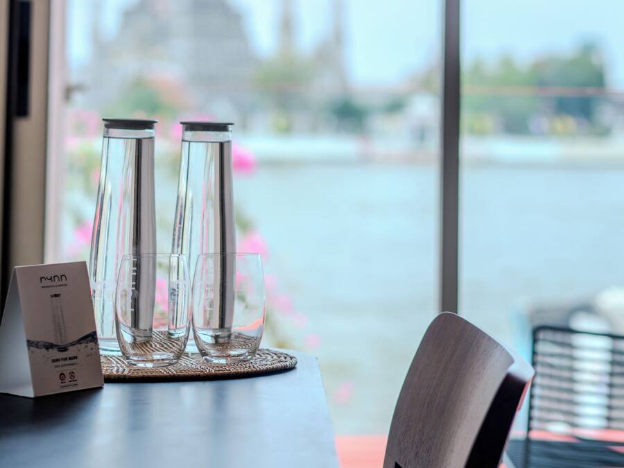 A table with two glasses and a menu, a chair, and a view of a temple through a window.