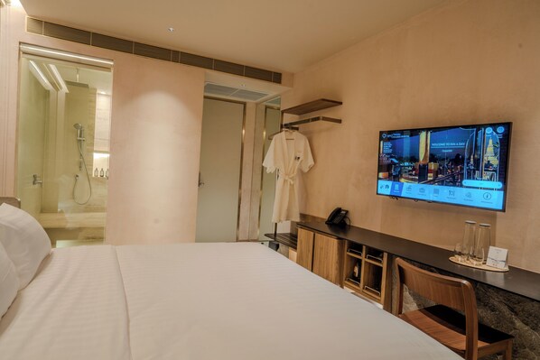 Una camera d'albergo con un letto, una TV a parete, un accappatoio su un appendiabiti e uno spazio doccia.