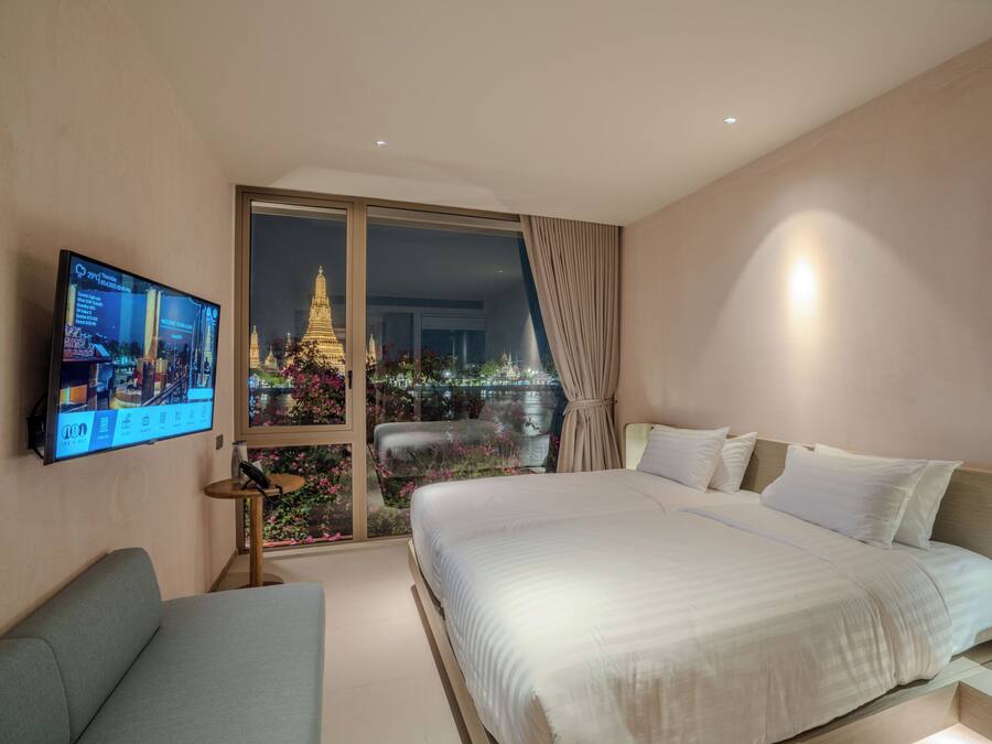 A modern hotel room with a large bed, a television on the wall, and a view of a temple through a glass door.
