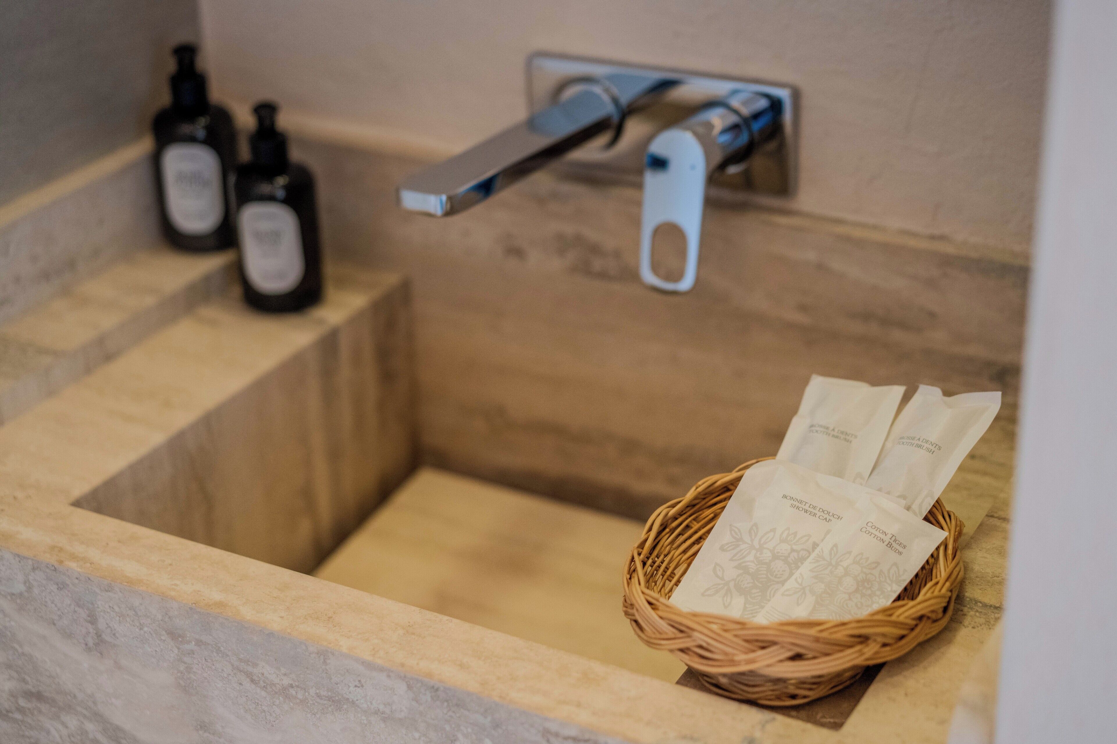 A bathroom with a wooden basin, a towel rack, and a basket with toiletries.
