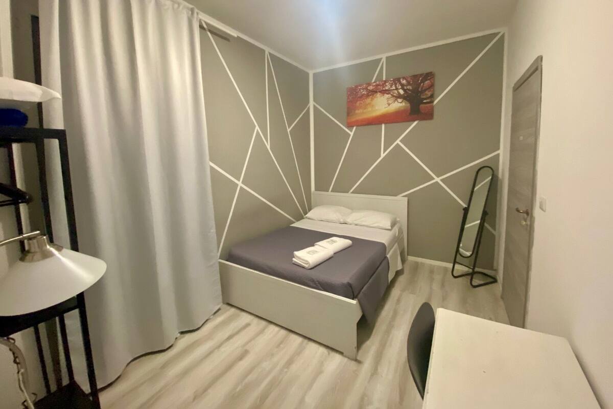 A modern bedroom with a bed, a bedside table, a lamp, and a painting on the wall.