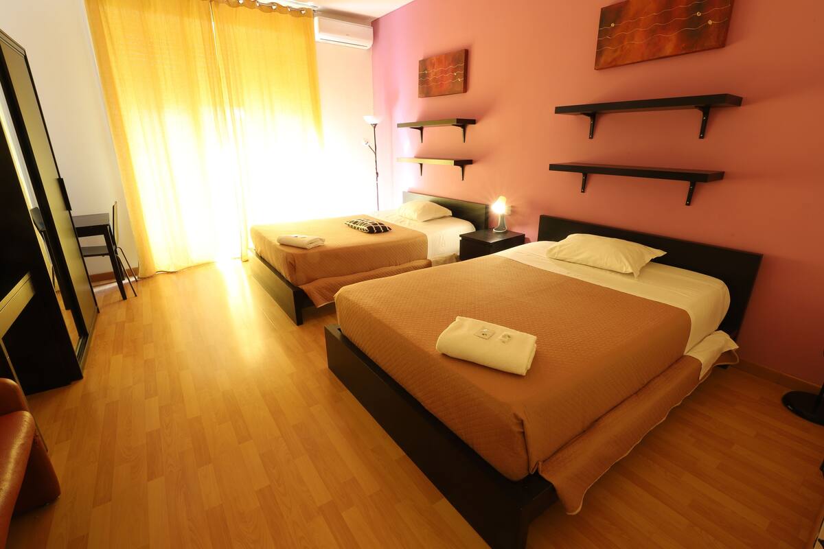 A hotel room with two beds, wooden flooring, a desk, and a chair.