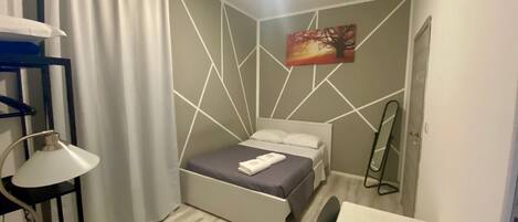 Un dormitorio pequeño con cama, escritorio, lámpara y un cuadro en la pared.