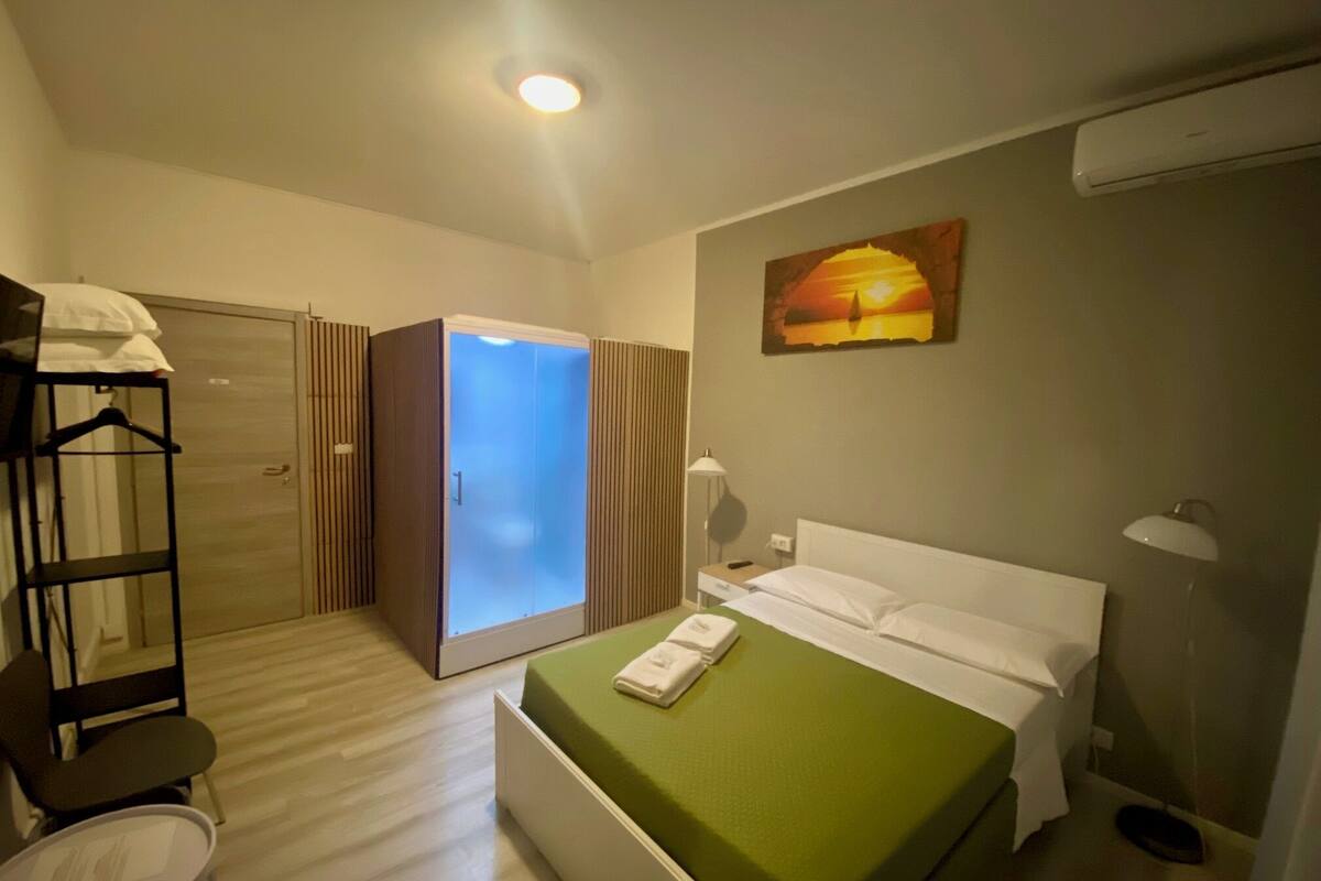 A hotel room with a bed, a wardrobe, a chair, a desk, and a painting on the wall.
