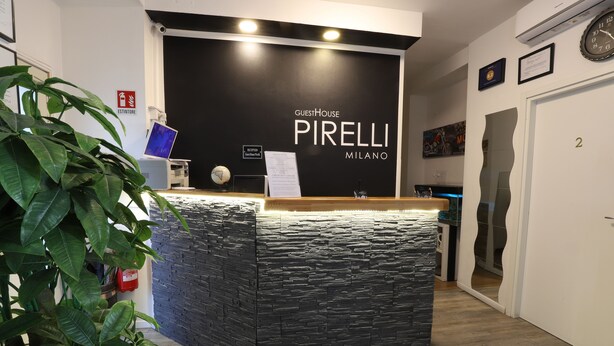 A reception desk with a black backdrop and the name "GuestHouse Pirelli Milano" displayed. - Guest House Pirelli (Milan)