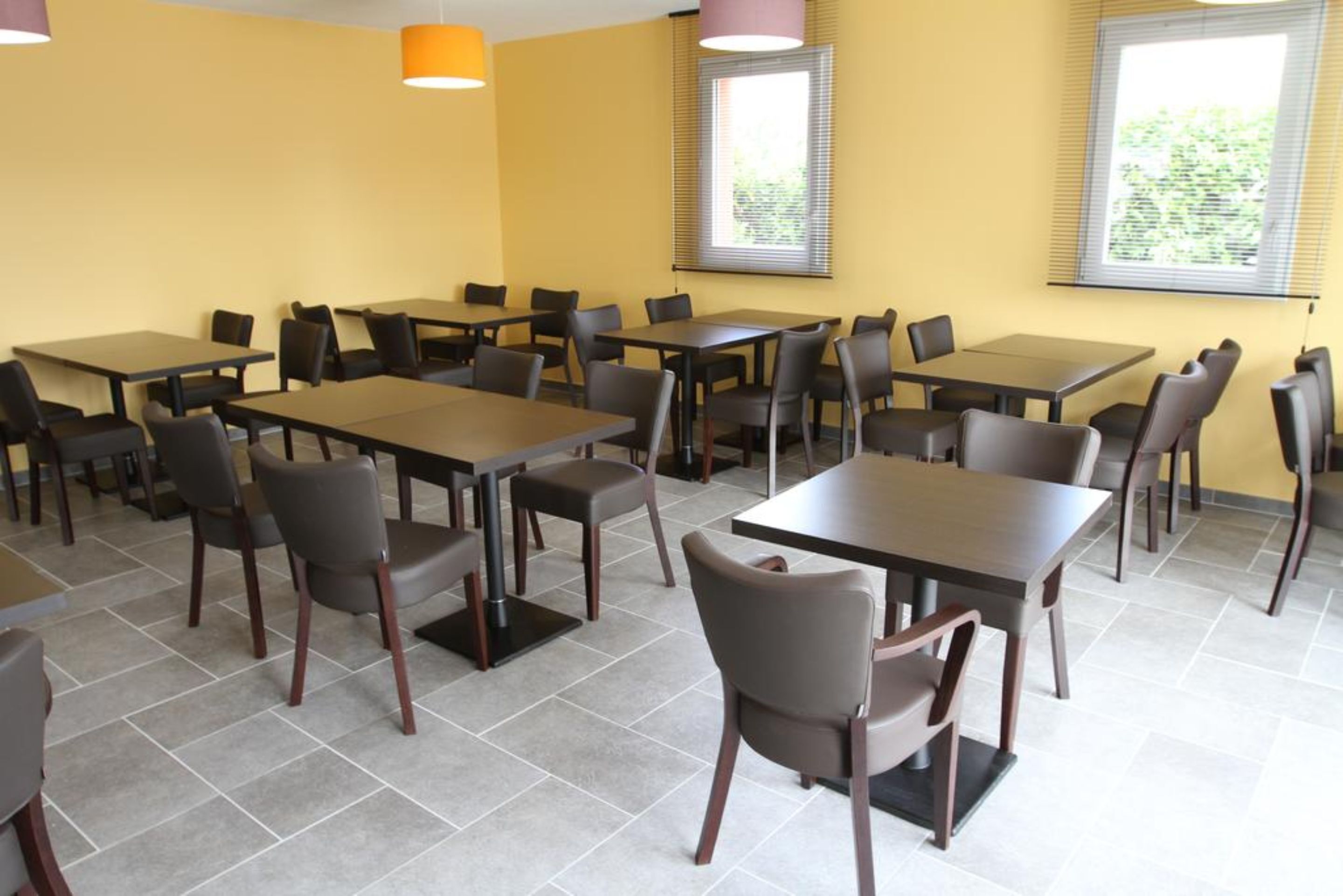 A conference room with multiple tables and chairs, yellow walls, and large windows with blinds.