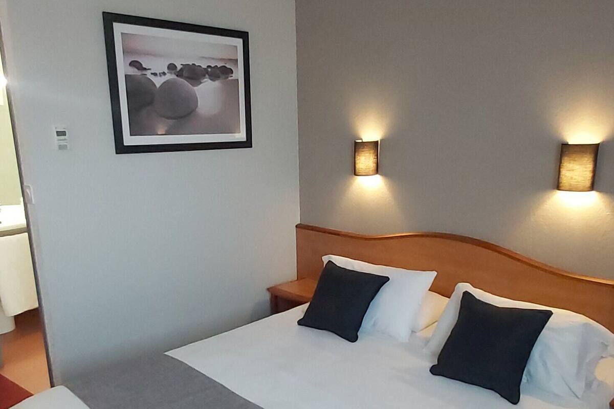 Ein Hotelzimmer mit einem großen Bett, einer Kopfteil, zwei Wandleuchten und einem gerahmten Bild an der Wand.