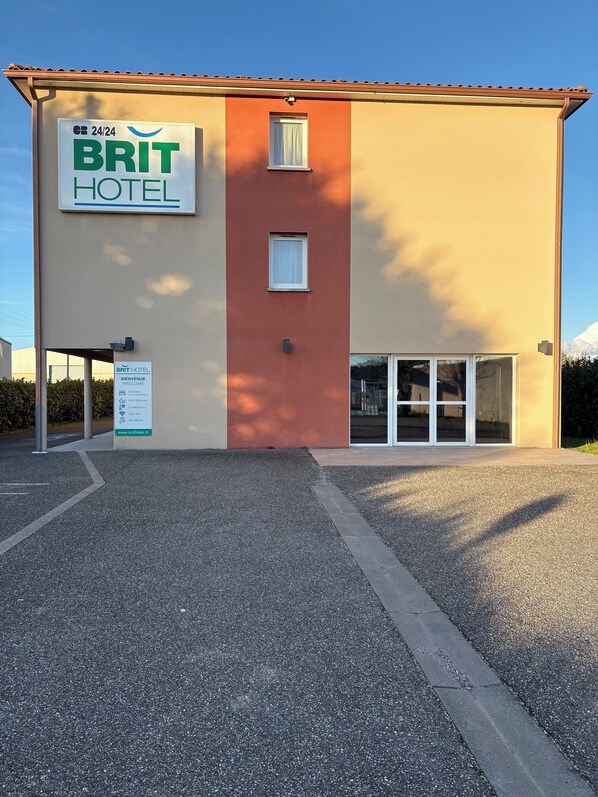 Edificio de BRIT HOTEL con un letrero de servicio 24/24, un cartel de bienvenida y una dirección web.