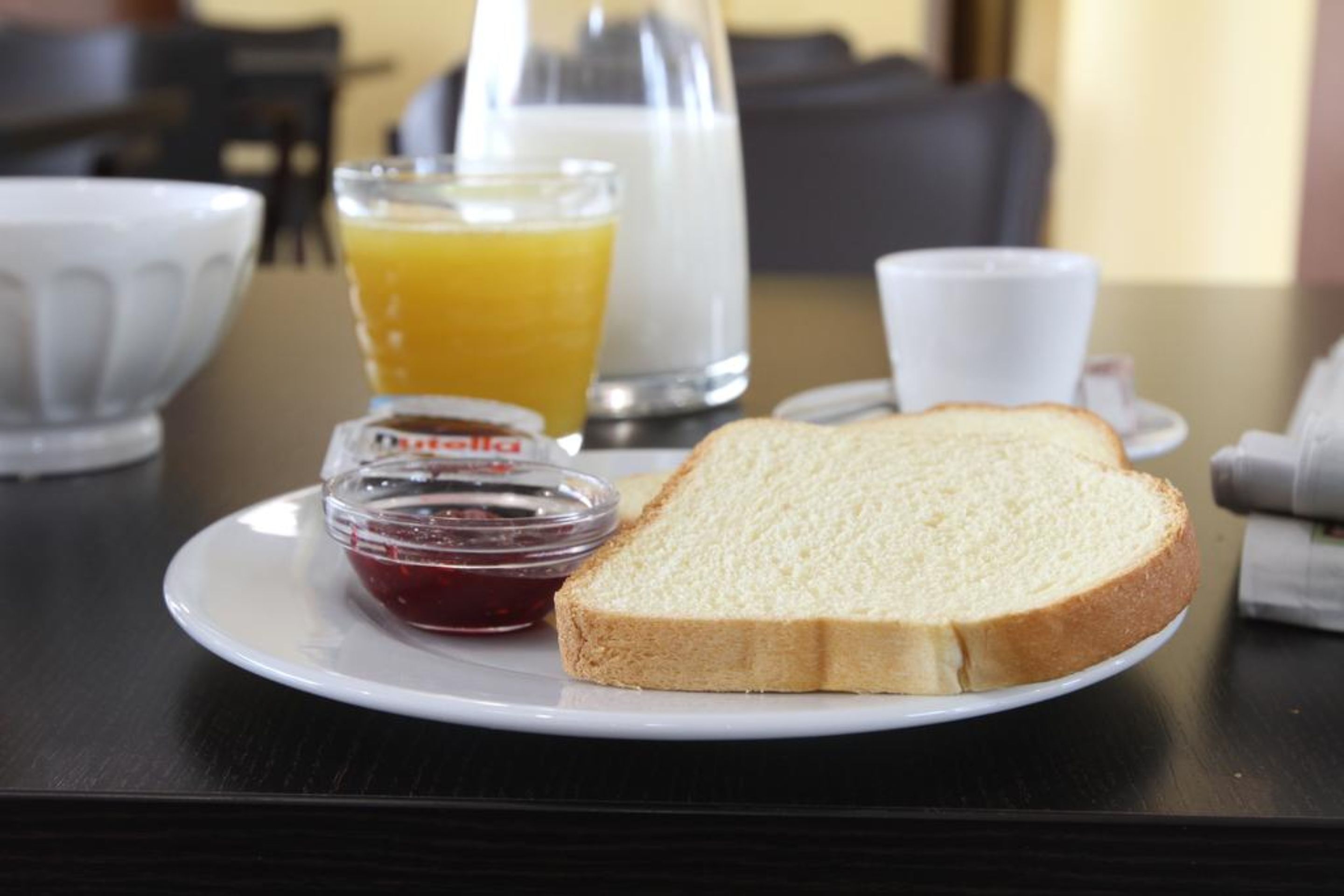Desayuno con tostadas, mermelada, jugo de naranja y leche sobre una mesa.