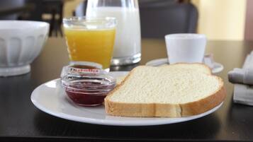 Desayuno con tostadas, mermelada, jugo de naranja y leche sobre una mesa.