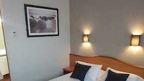 Quarto de hotel com uma cama grande, um cobertor cinza, duas luminárias de cabeceira e um quadro na parede.