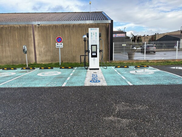 Un espace de stationnement équipé de bornes de recharge pour véhicules électriques, un panneau indiquant l’interdiction de se garer et un bâtiment en arrière-plan.