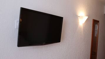 A flat-screen TV mounted on a textured wall with a wall-mounted light fixture to the right.