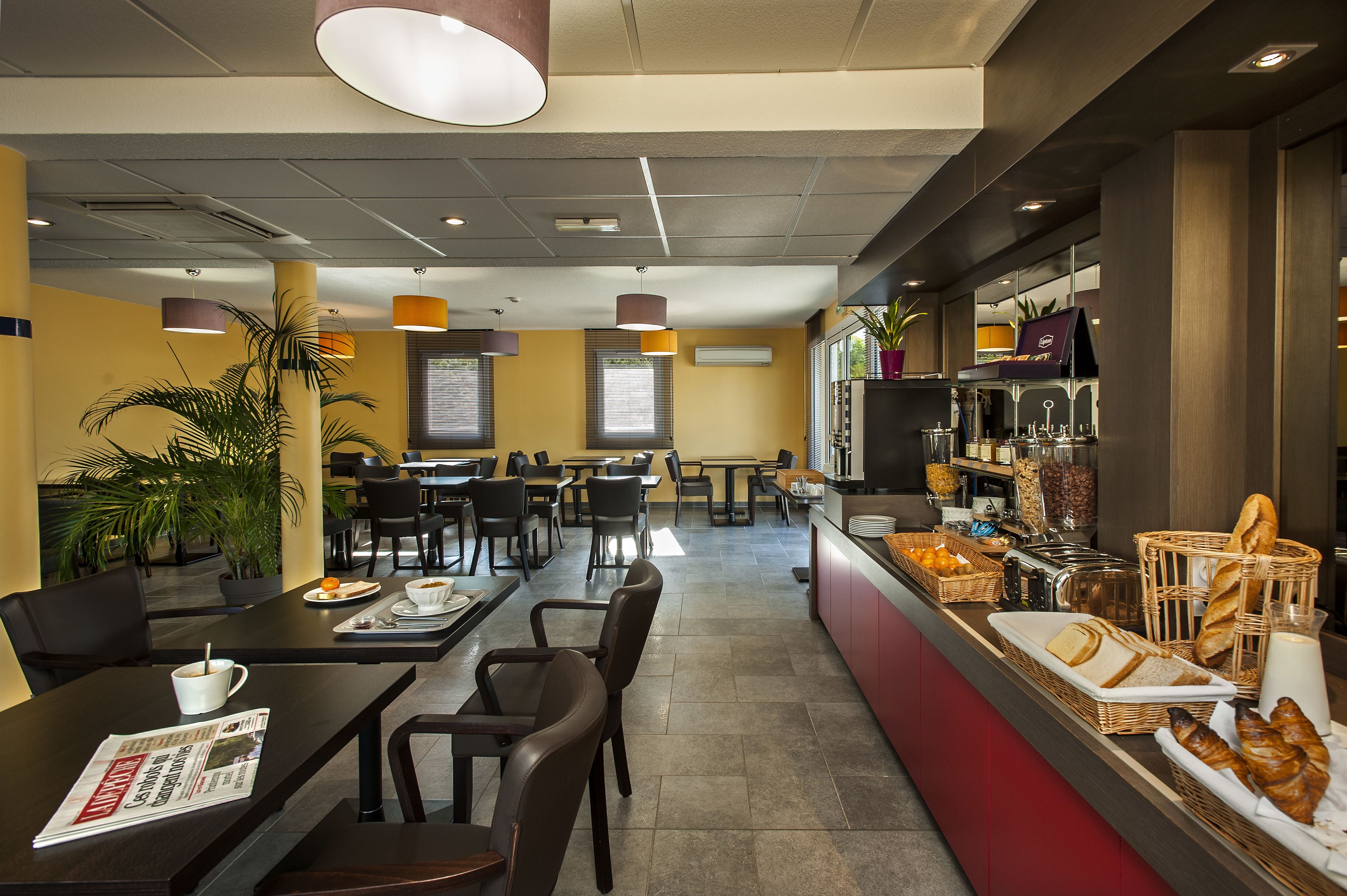 Un café moderno con varias zonas de estar, una barra con opciones de desayuno y una máquina de café a la vista.