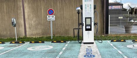 Una estación de carga con un cartel que indica cargador de vehículo eléctrico de 120 kW, un letrero de no estacionamiento y una señal de flecha direccional.