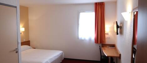 Habitación de hotel con cama, escritorio, silla, ventana con cortinas y televisión montada en la pared.