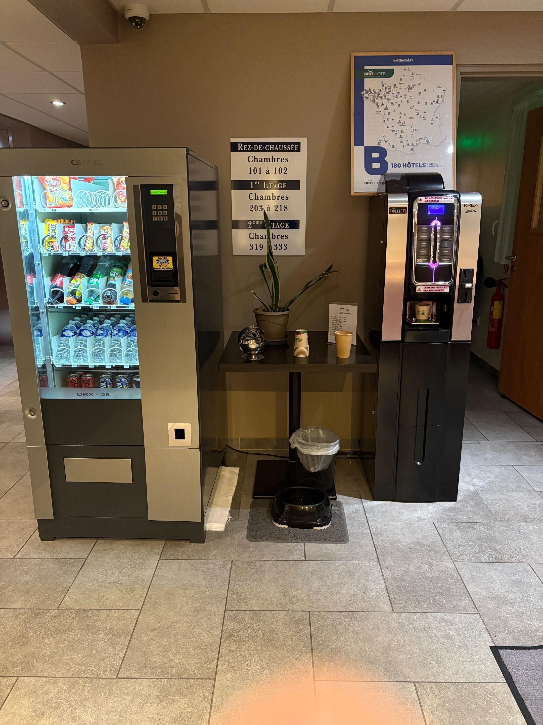 A hotel reception area with a vending machine, a self-service coffee machine, and a map of the hotel.