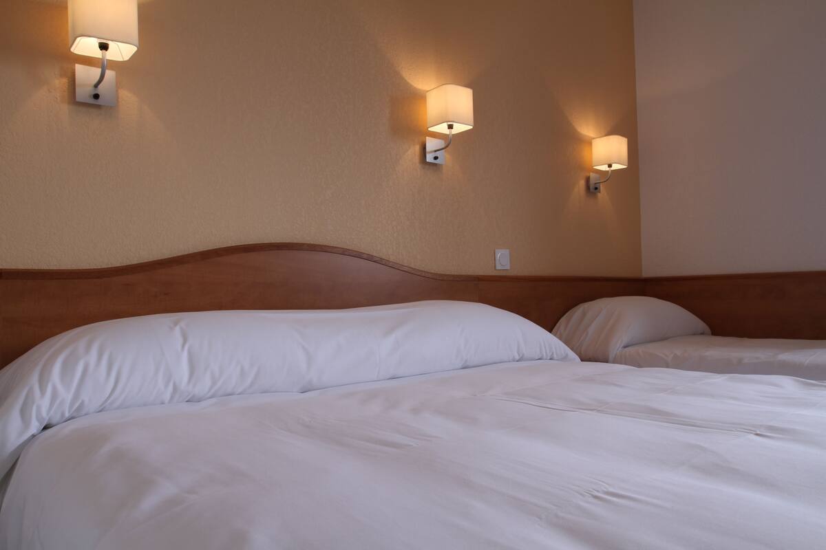 Ein Hotelzimmer mit zwei Betten, jeweils mit weißer Bettwäsche, und Wandleuchten, die für eine stimmungsvolle Beleuchtung sorgen.