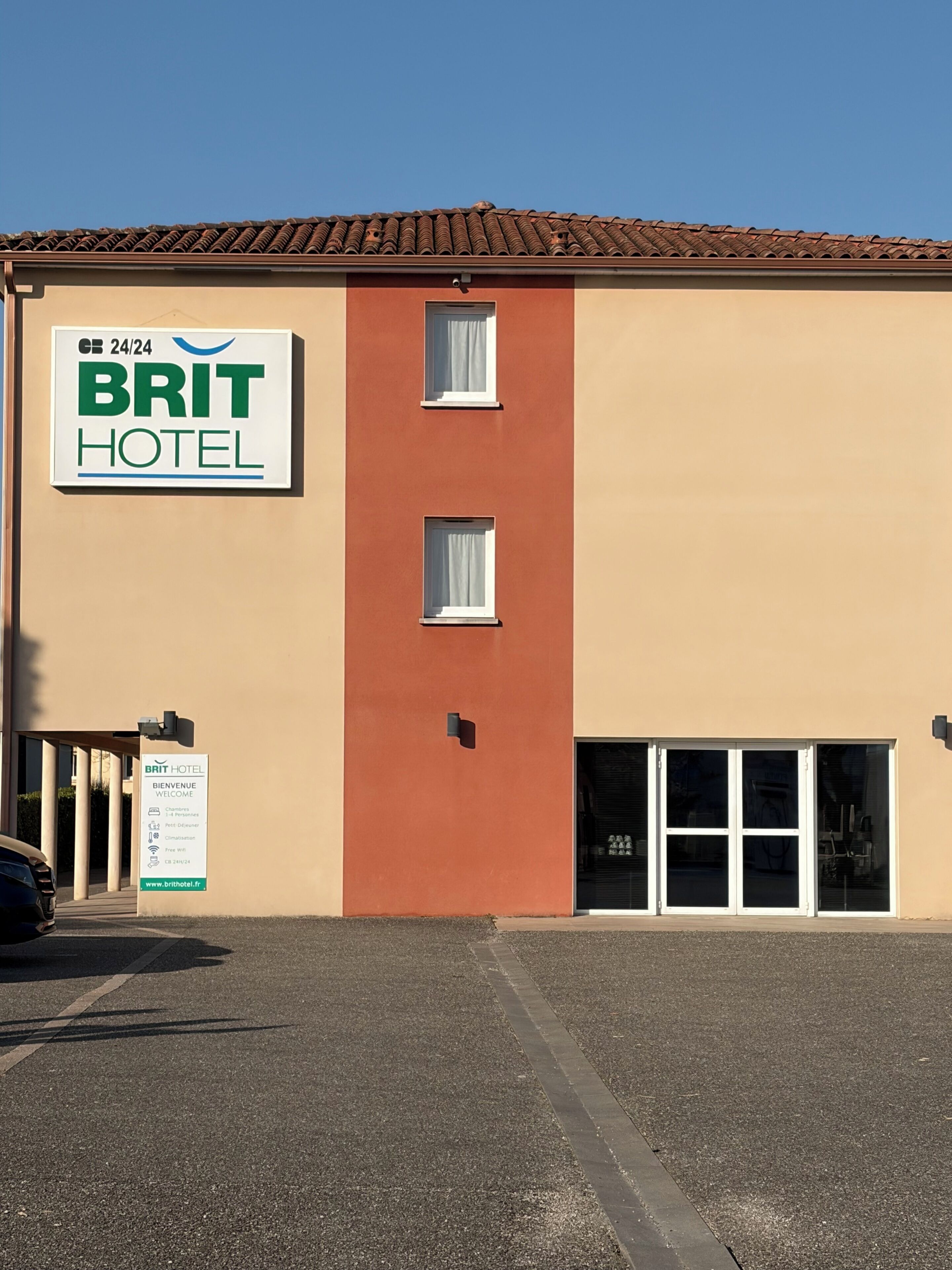 Ein BRIT HOTEL mit Schild für einen 24-Stunden-Service, einem Willkommensschild und einem Parkplatz.