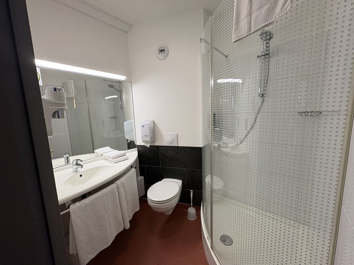 A modern bathroom with a white sink, mirror, toilet, and a glass-enclosed shower area.