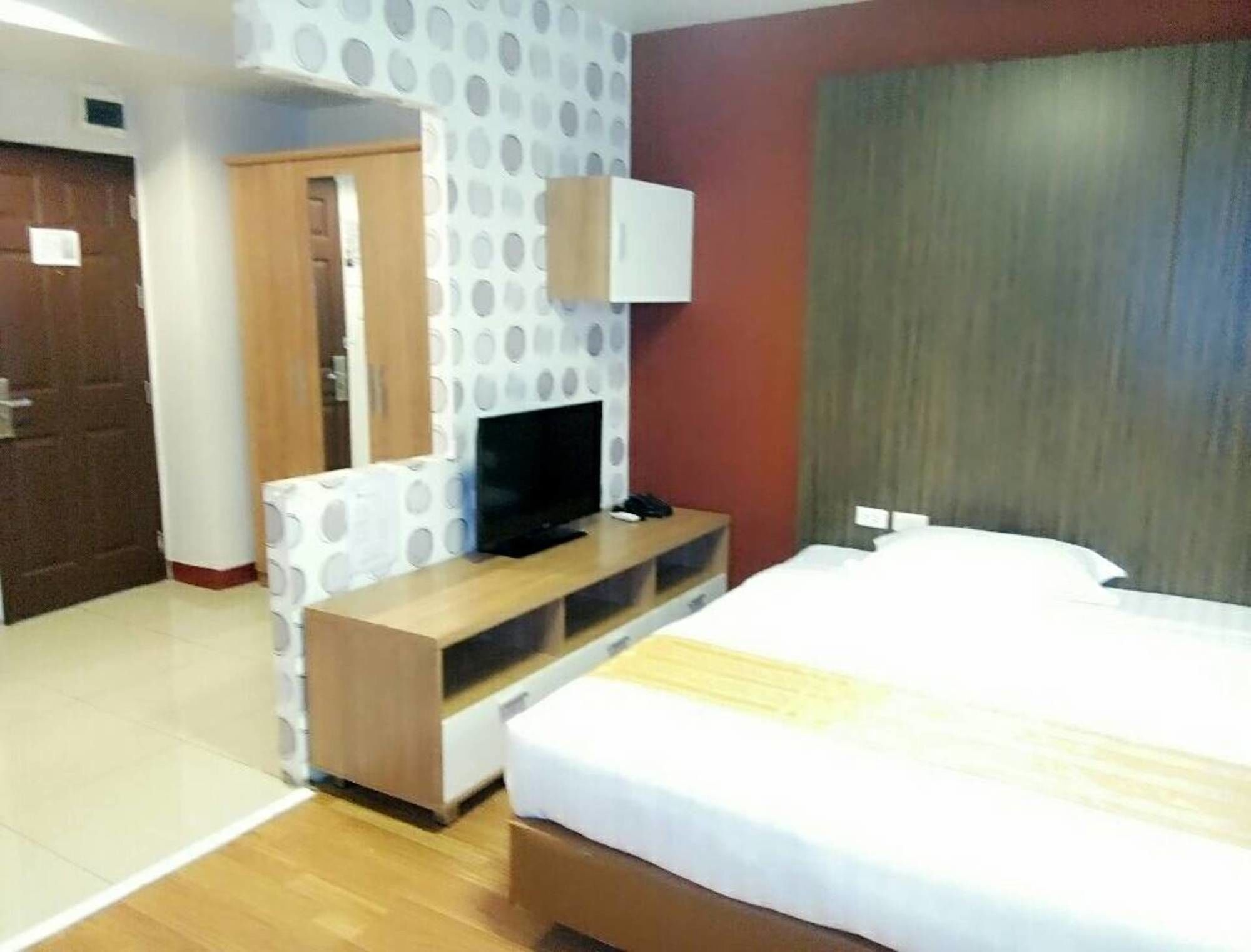 A hotel room with a bed, a TV on a wooden stand, a wardrobe, and a door.