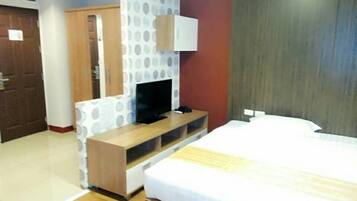 A hotel room with a bed, a TV on a wooden stand, a wardrobe, and a door.