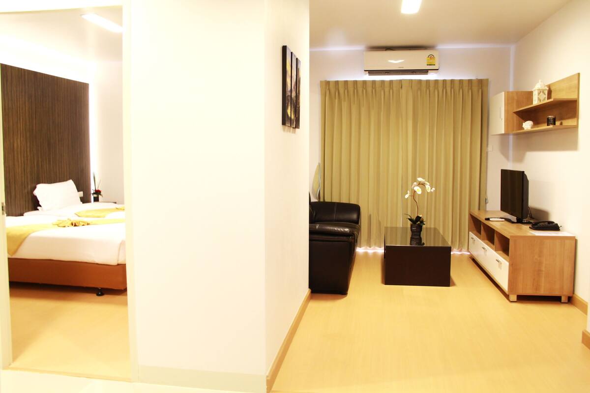 A hotel room with a bed, a desk, a chair, a TV, and a window with curtains.