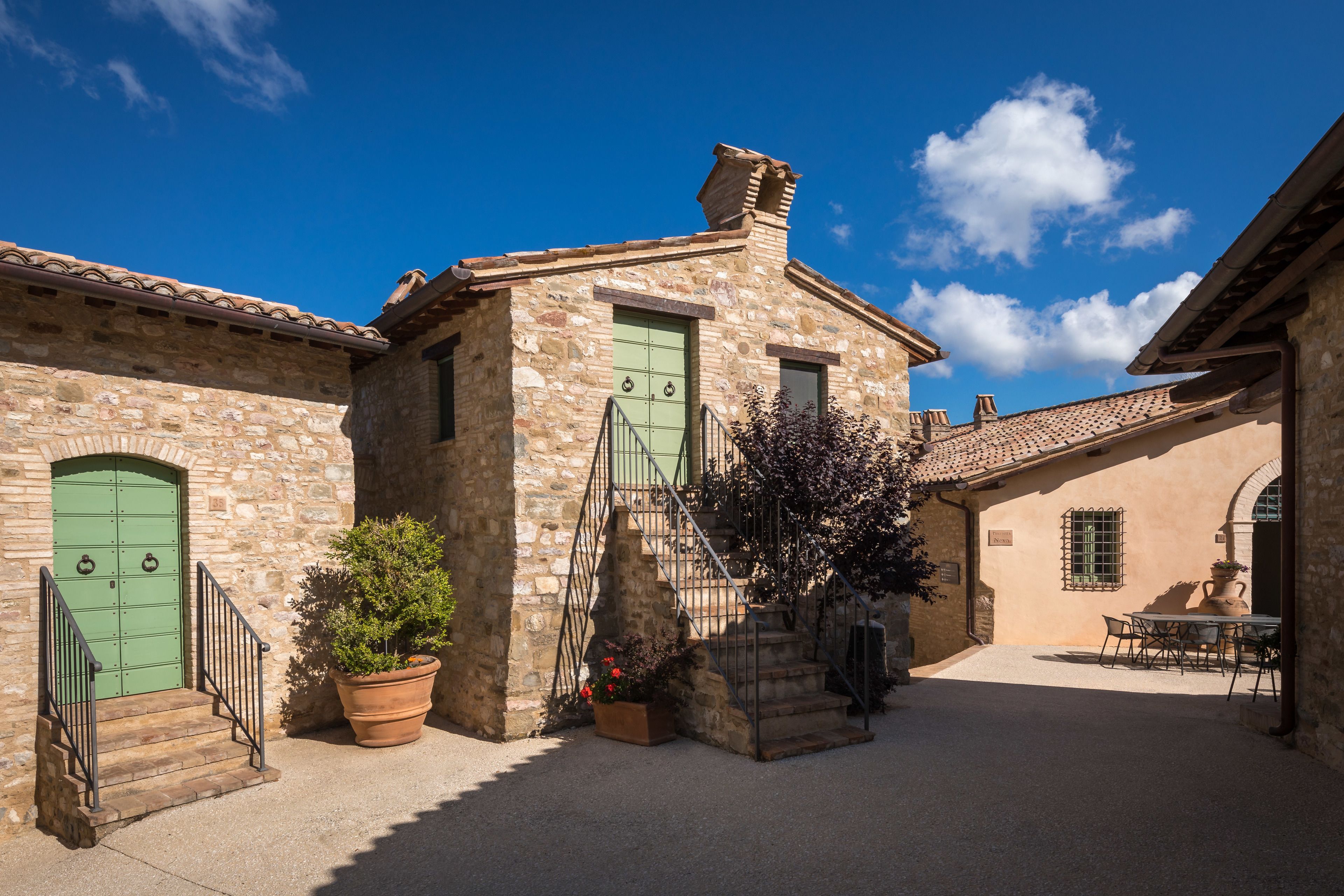 Un bâtiment en pierre avec une porte verte, un escalier et un patio aménagé avec une table et des chaises.