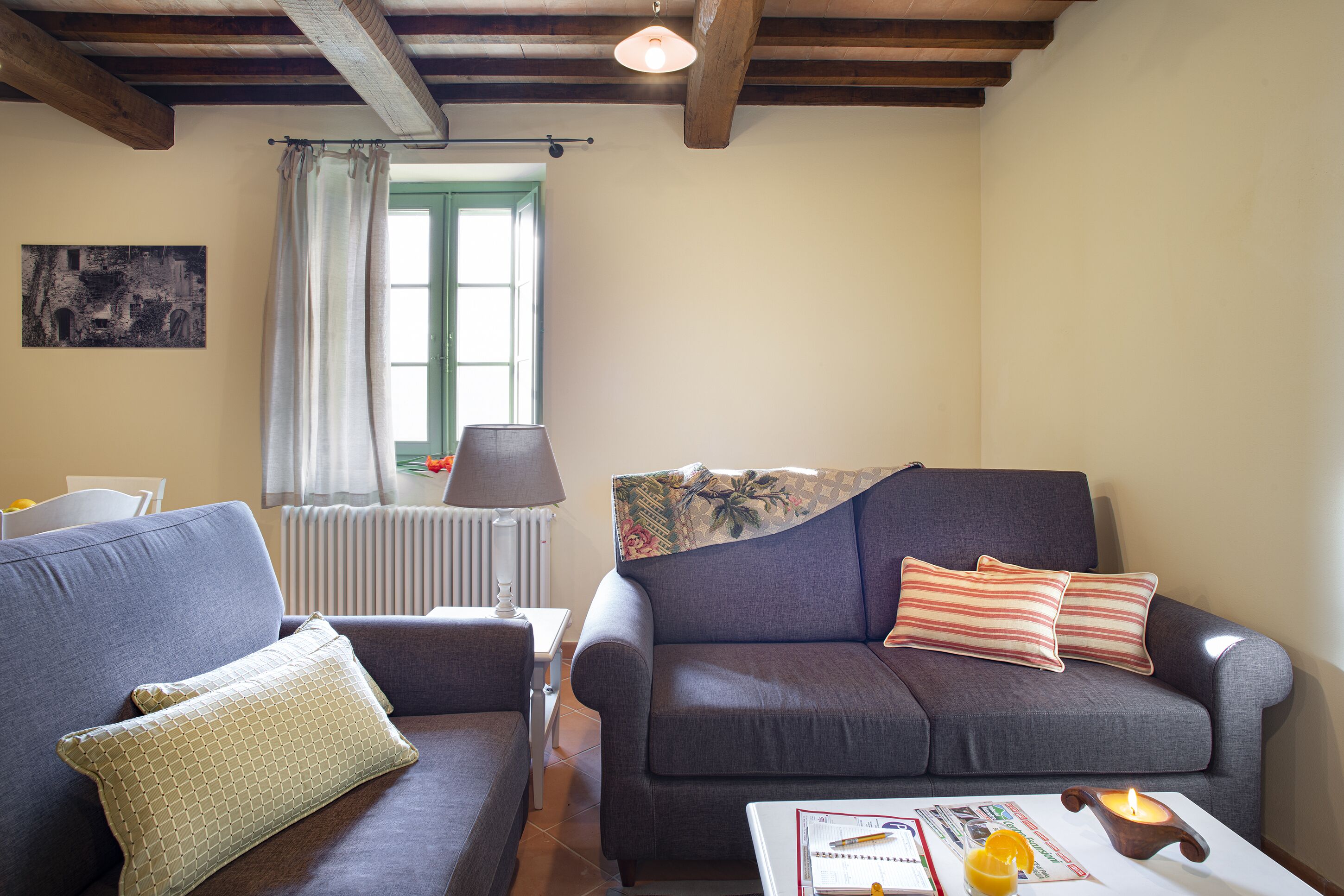 A living room with a sofa, a table with a candle, and a window with curtains.