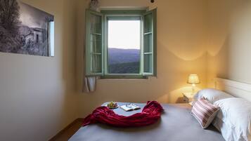 Une chambre à coucher avec un lit, une fenêtre dont les volets sont ouverts, une table de chevet avec une lampe et un tableau accroché au mur.