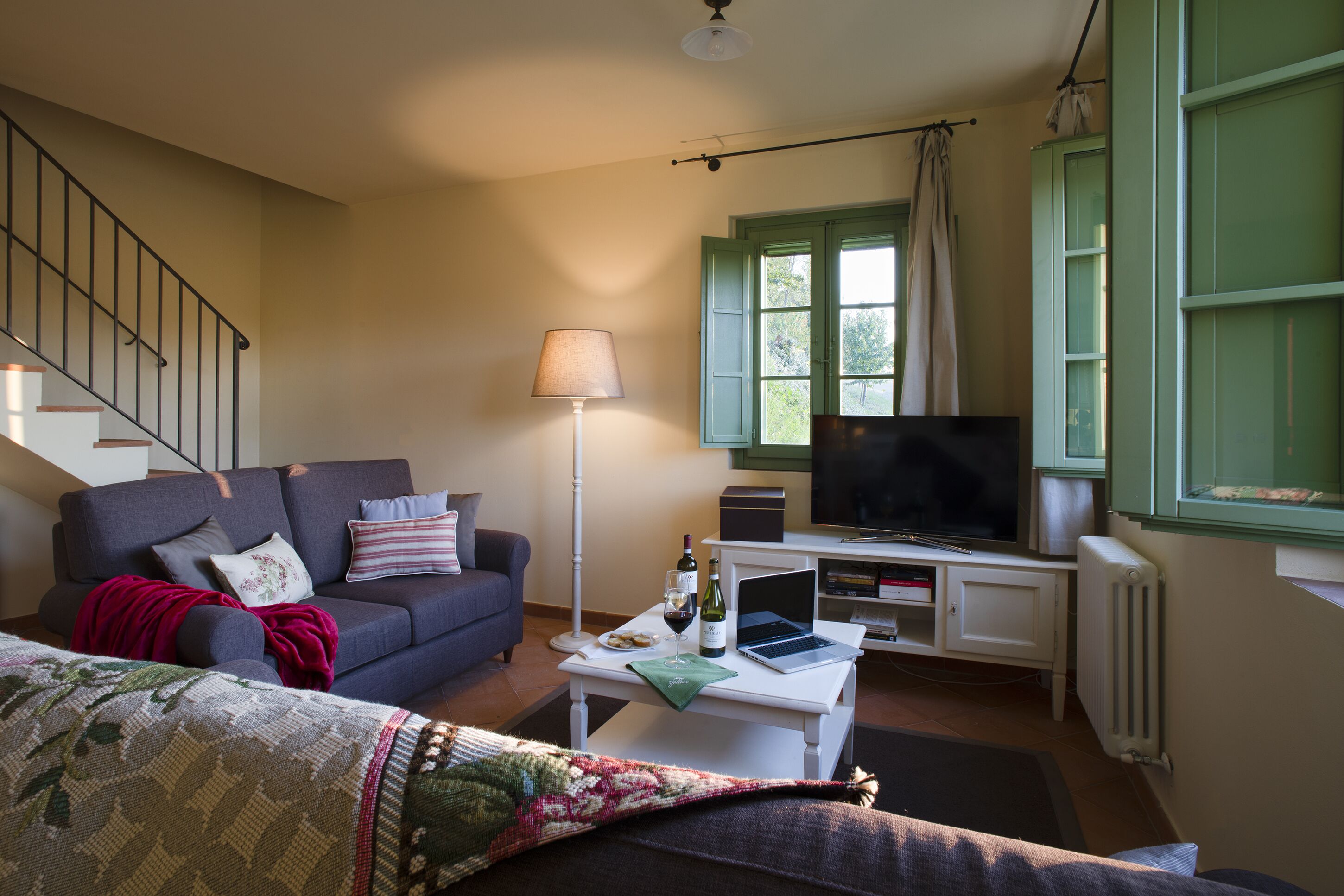 Ein Wohnzimmer mit einer Couch, einem Couchtisch mit Laptop und Wein, einem Fernseher und einer Treppe.