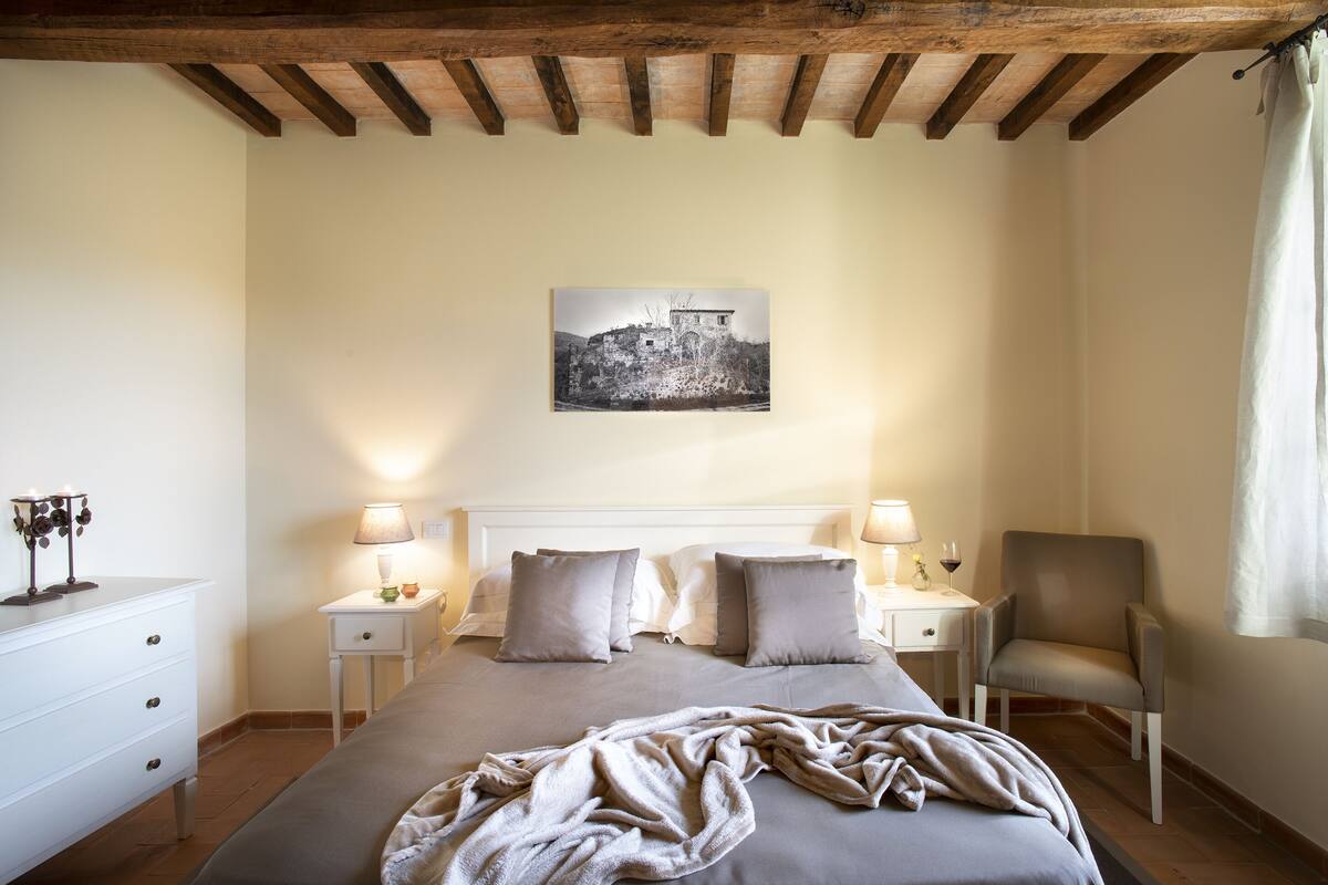 A bedroom with a bed, bedside tables, a chair, a lamp, and a painting on the wall.