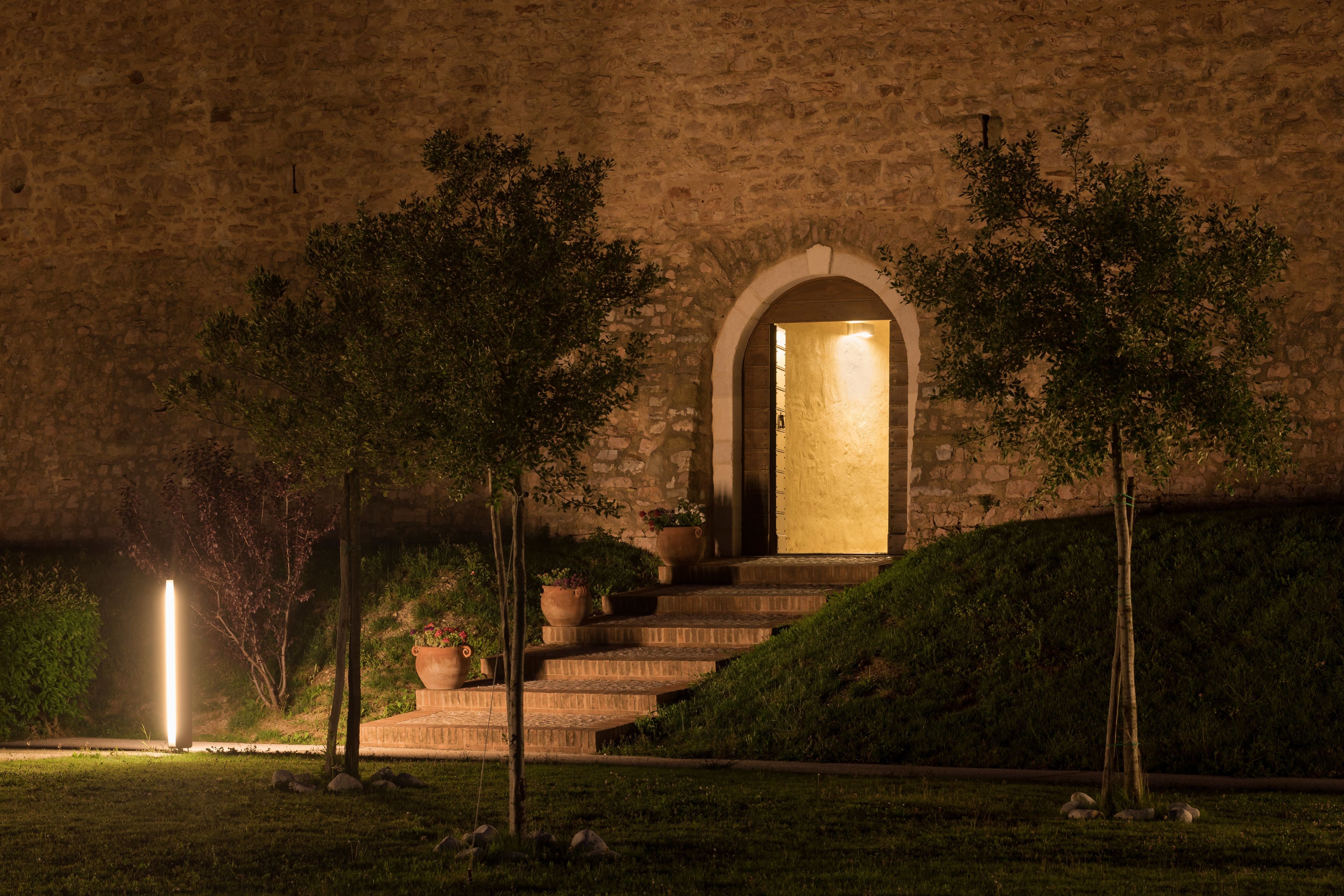 Edifici de pedra amb un portal d'arc central, escales que hi condueixen i plantes en testos a les escales.