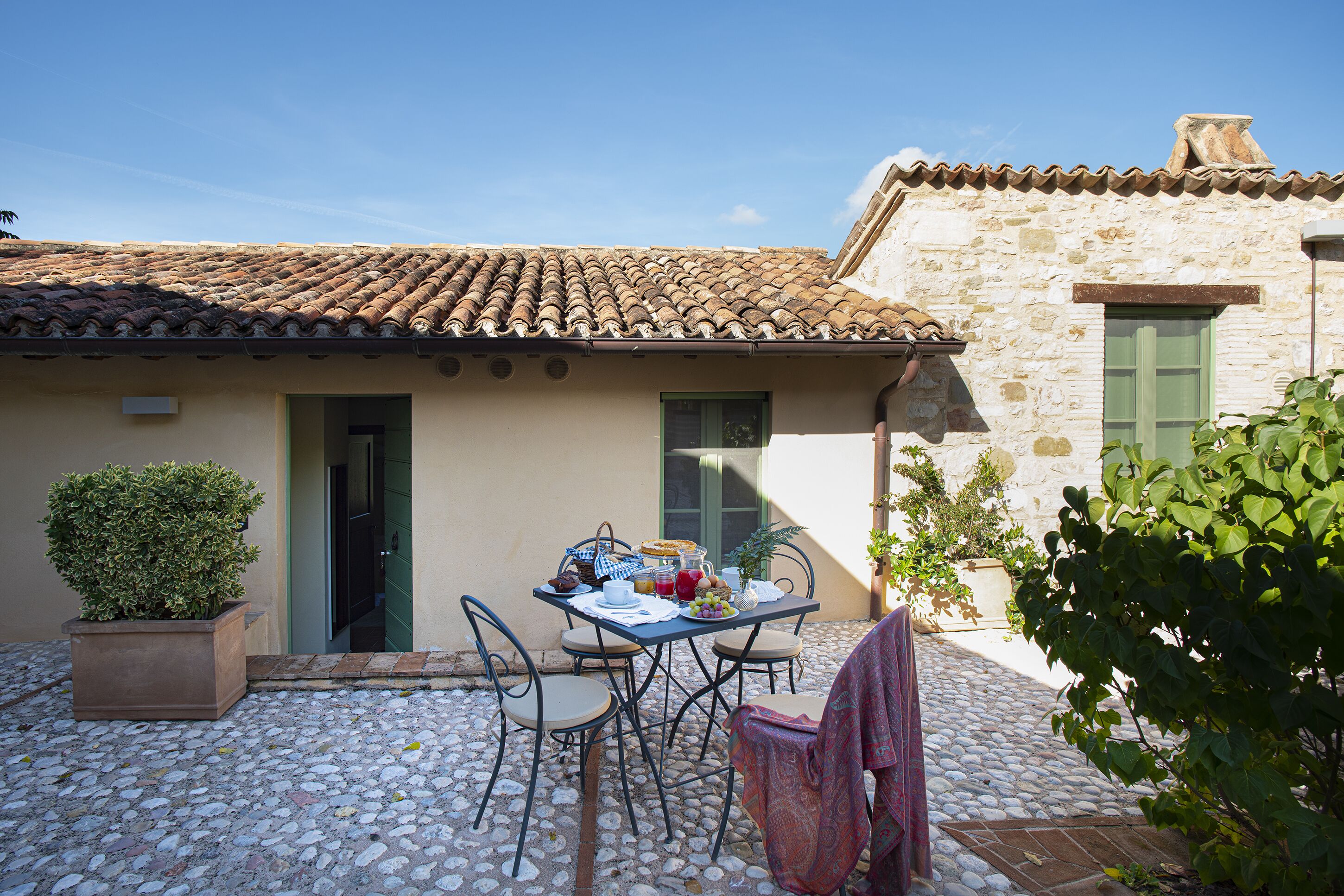 A stone building with a tiled roof, a patio with a table set for a meal, and potted plants.