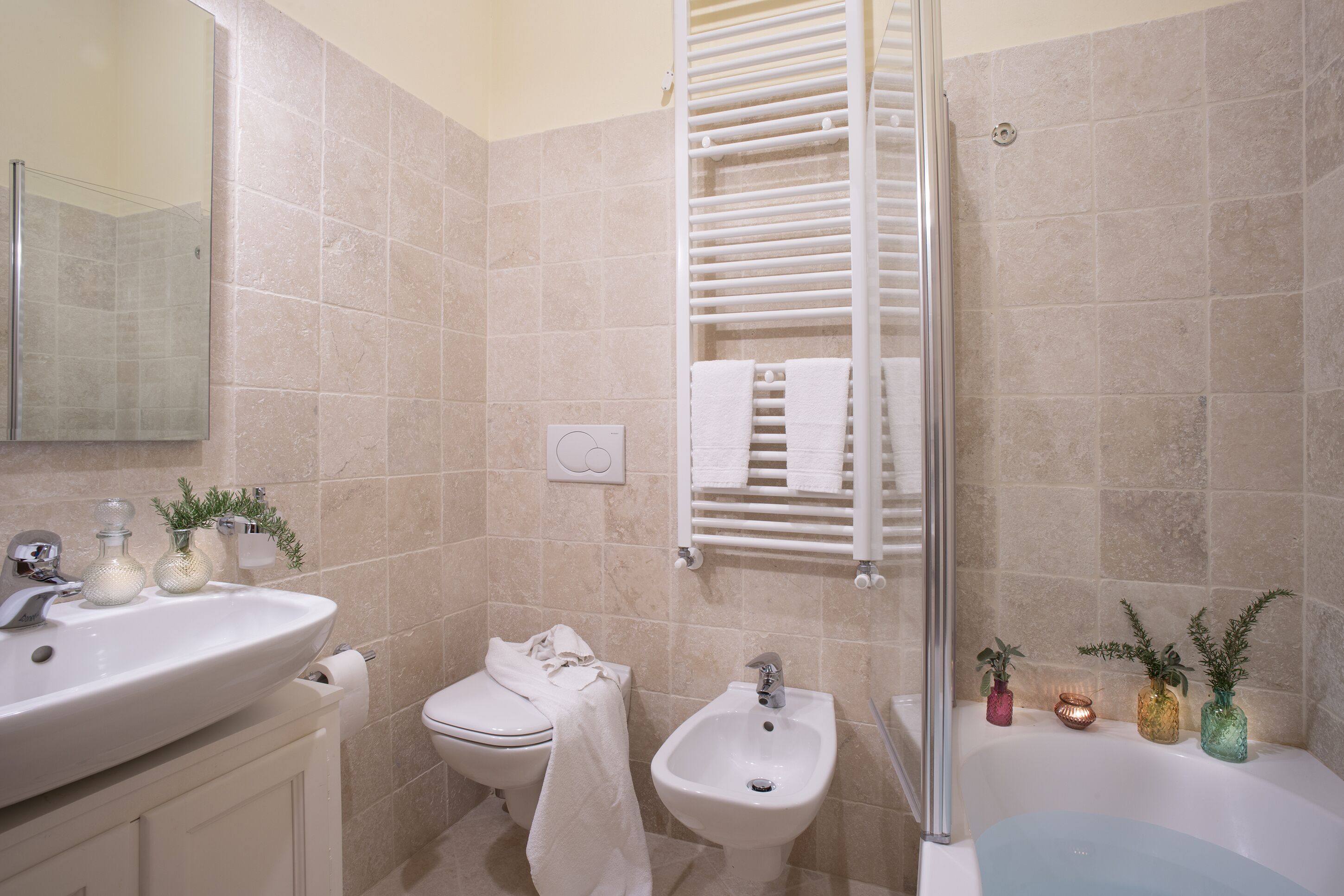 Une salle de bain équipée d’un lavabo, de toilettes, d’un bidet et d’une baignoire. On y trouve également des serviettes et des plantes décoratives.