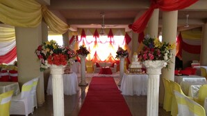 Un salón de banquetes con pasillo de alfombra roja, columnas blancas y sillas amarillas.