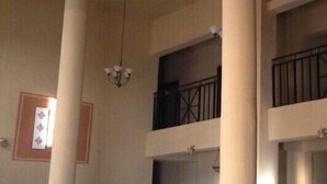Un interior de varios niveles con columnas, una escalera y un balcón con barandilla de hierro forjado.