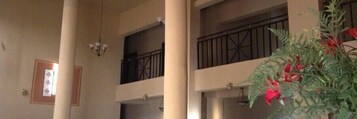 Un interior de varios niveles con columnas, una escalera y un balcón con barandilla de hierro forjado.