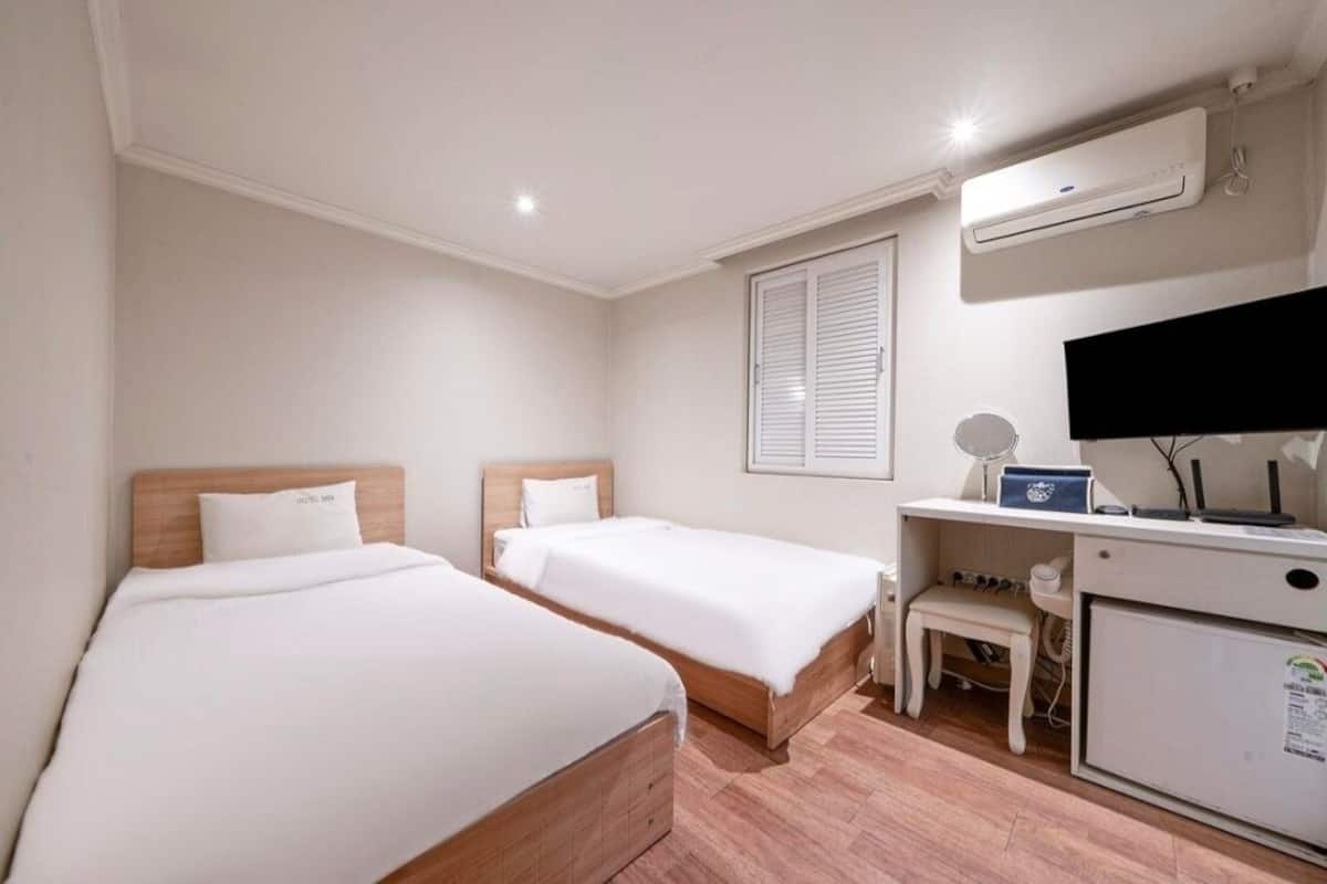 A hotel room with two single beds, a desk with a computer, a TV, and a small refrigerator.