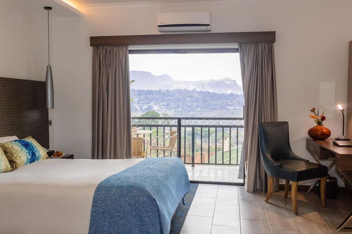 A hotel room with a bed, a desk, a chair, and a balcony with a view.